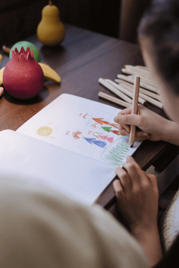 Child drawing in notebook with colored pencils